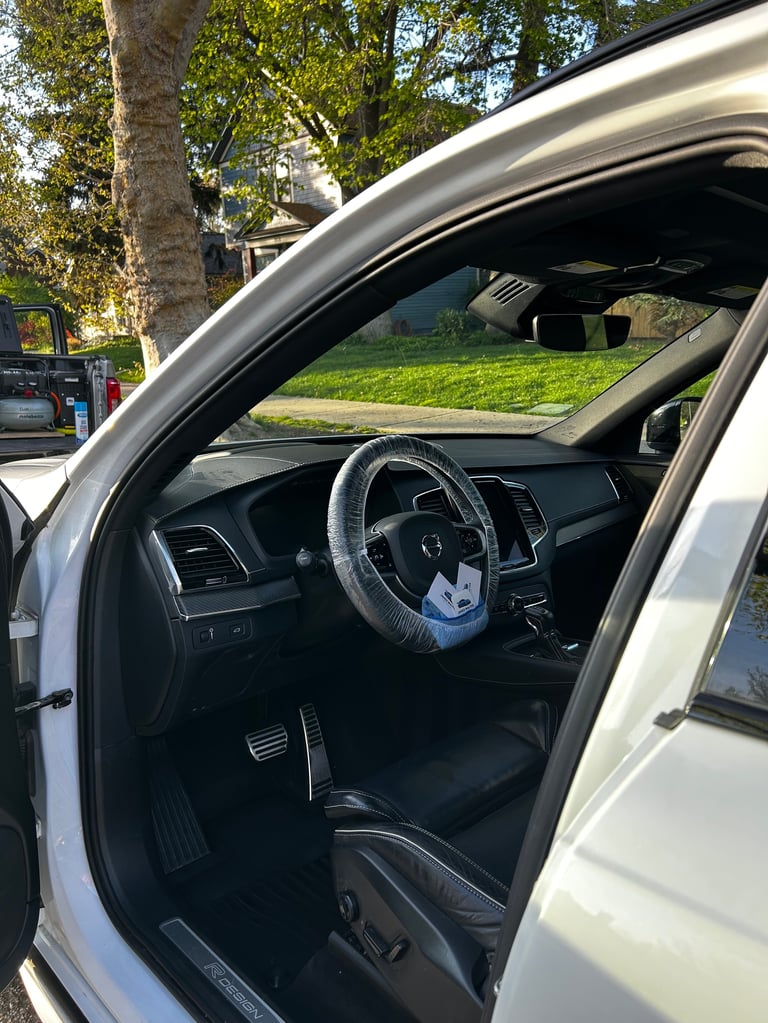 Interior view of white car with open door showing steering wheel and dark dashboard on sunny day