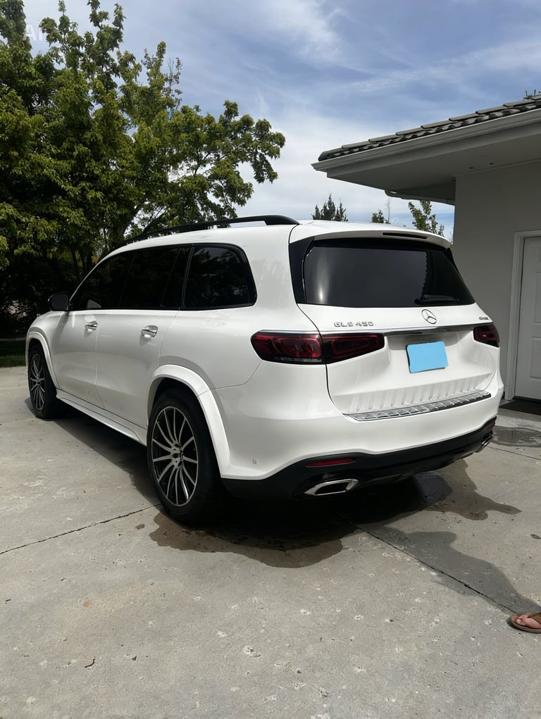 White Mercedes-Benz GLE SUV parked in driveway with garage, rear three-quarter view on sunny day