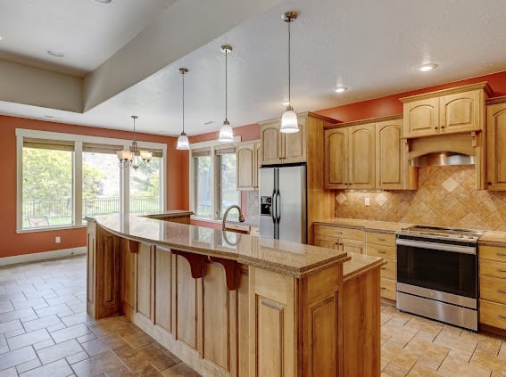 Spacious kitchen with orange walls, wooden cabinets, large island with seating, stainless steel appliances, and pendant lighting