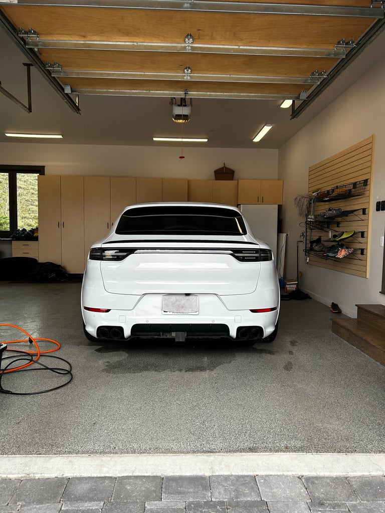 White sports car parked in a modern garage with wooden beams, cabinets, and tools on the wall