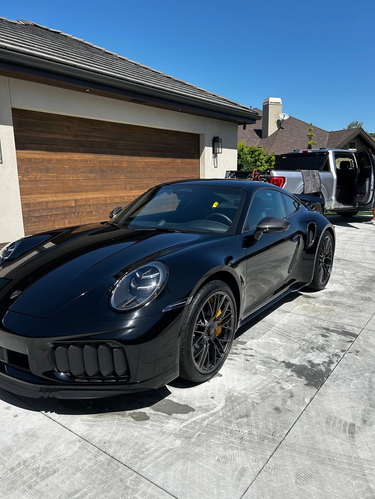Black Porsche sports car parked in driveway of modern home with wooden garage door