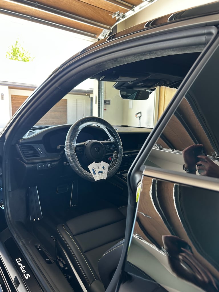 Interior view of a classic car with open door showing steering wheel, dashboard, and brown leather seats