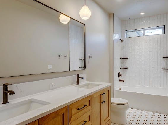 Modern bathroom with wooden vanity, white countertop, large mirror, pendant lights, and tiled shower area with tub