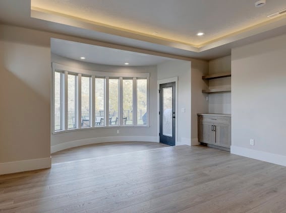 Empty modern living room with bay window, hardwood floors, recessed ceiling lights, and built-in shelving