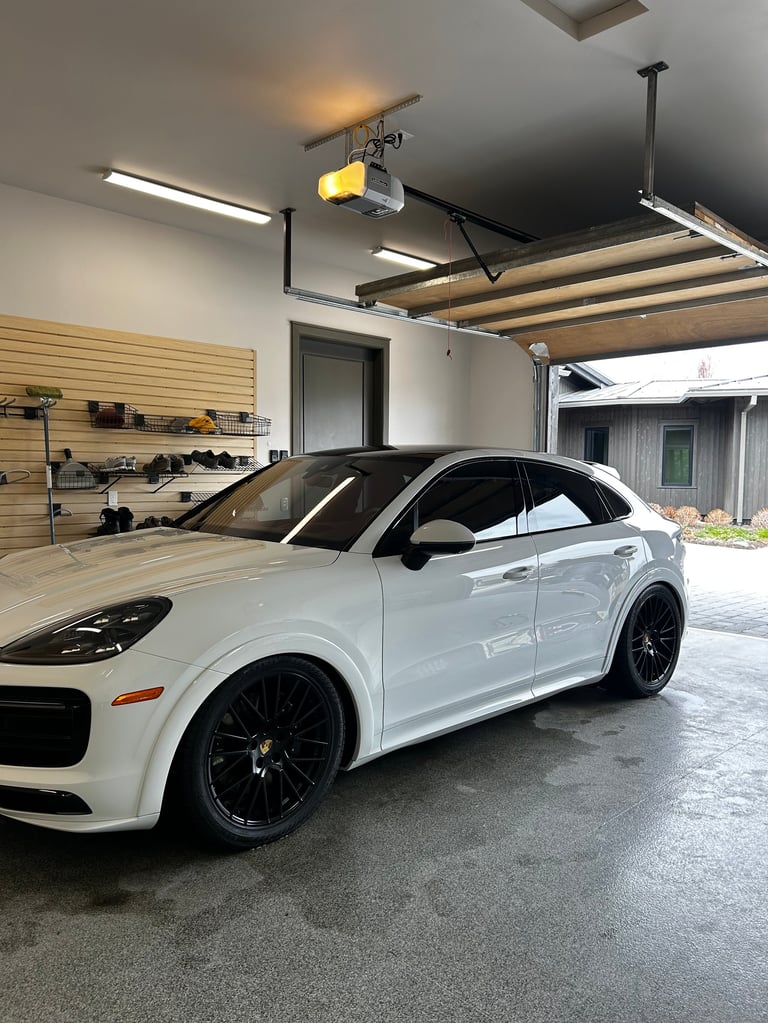 White Porsche Cayenne parked in modern garage with wooden wall shelving and work lights overhead