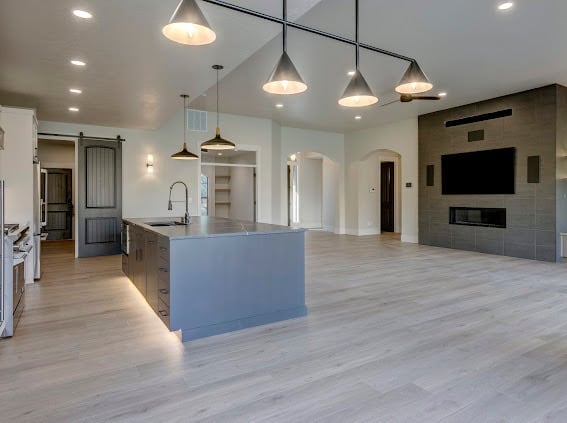 Modern open-concept kitchen and living room with blue island, pendant lights, wood flooring, and built-in TV wall