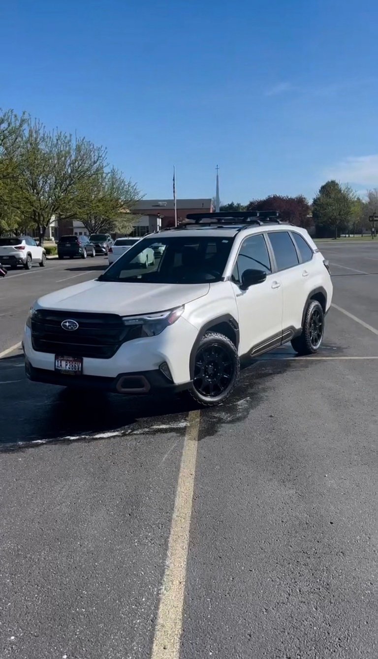 White Subaru SUV parked in an empty parking lot on a clear sunny day