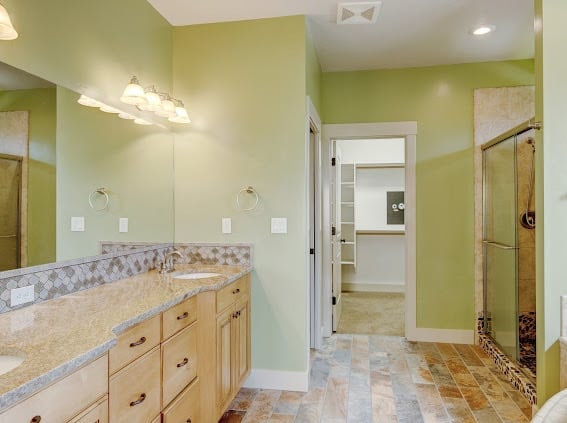 Modern bathroom with green walls, double vanity with light wood cabinets, granite countertop, and glass walk-in shower