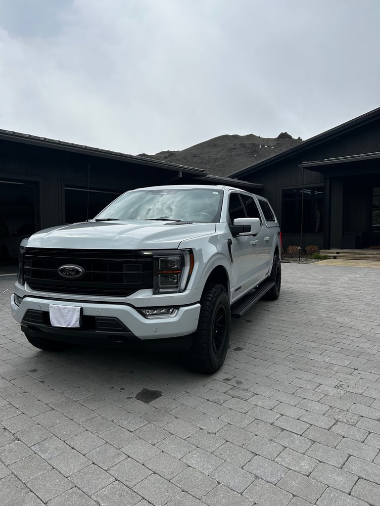 White Ford Expedition SUV parked on paved driveway in front of modern black garage structure with mountain backdrop