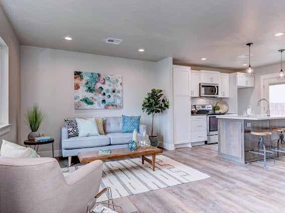 Modern open-concept living room and kitchen with light blue sofa, colorful abstract art, and white cabinetry