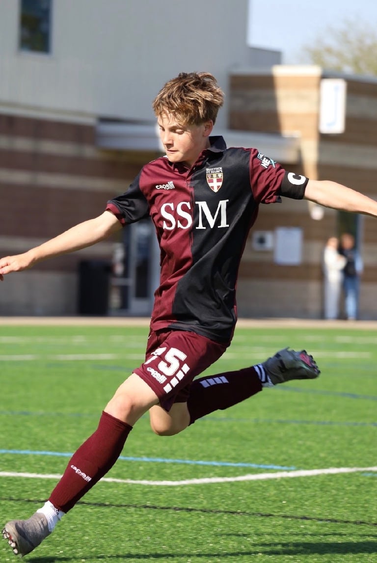 Young soccer player in maroon and black SSM jersey performing a kicking motion on grass field