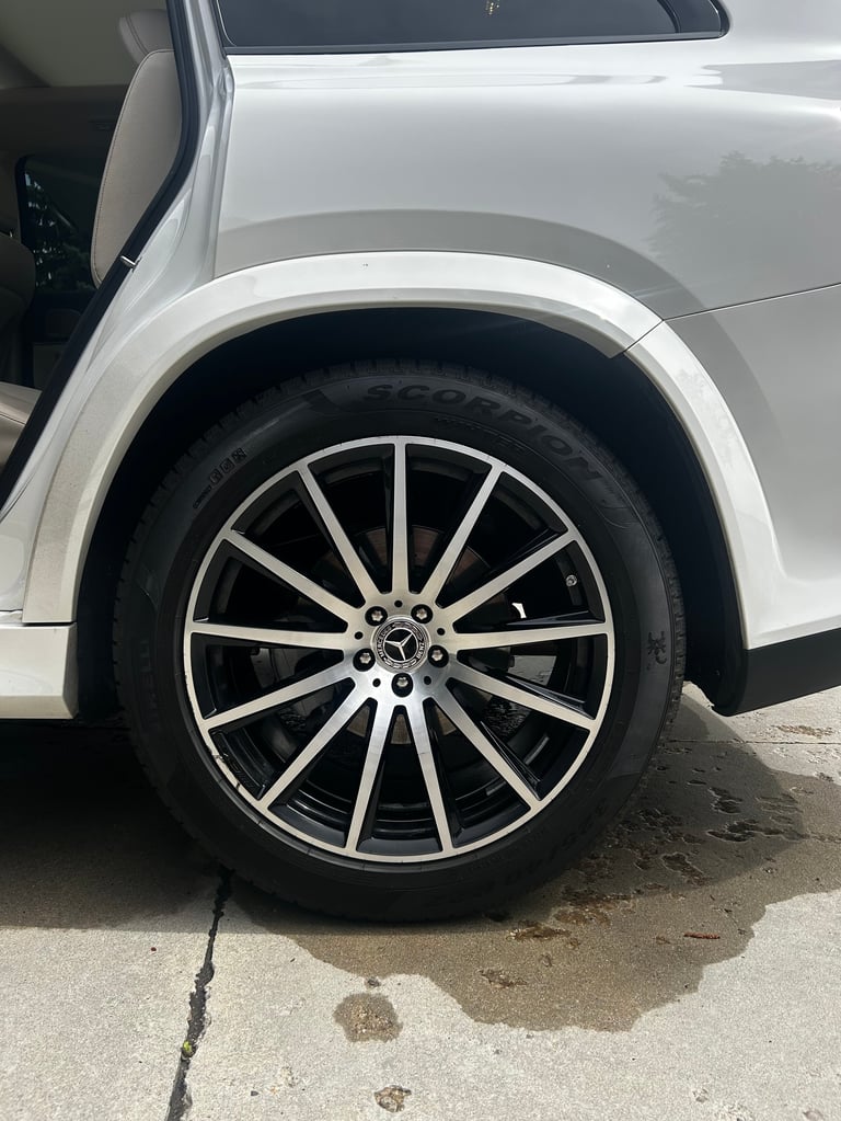 White vehicle wheel with multi-spoke alloy rim and black tire against white car body