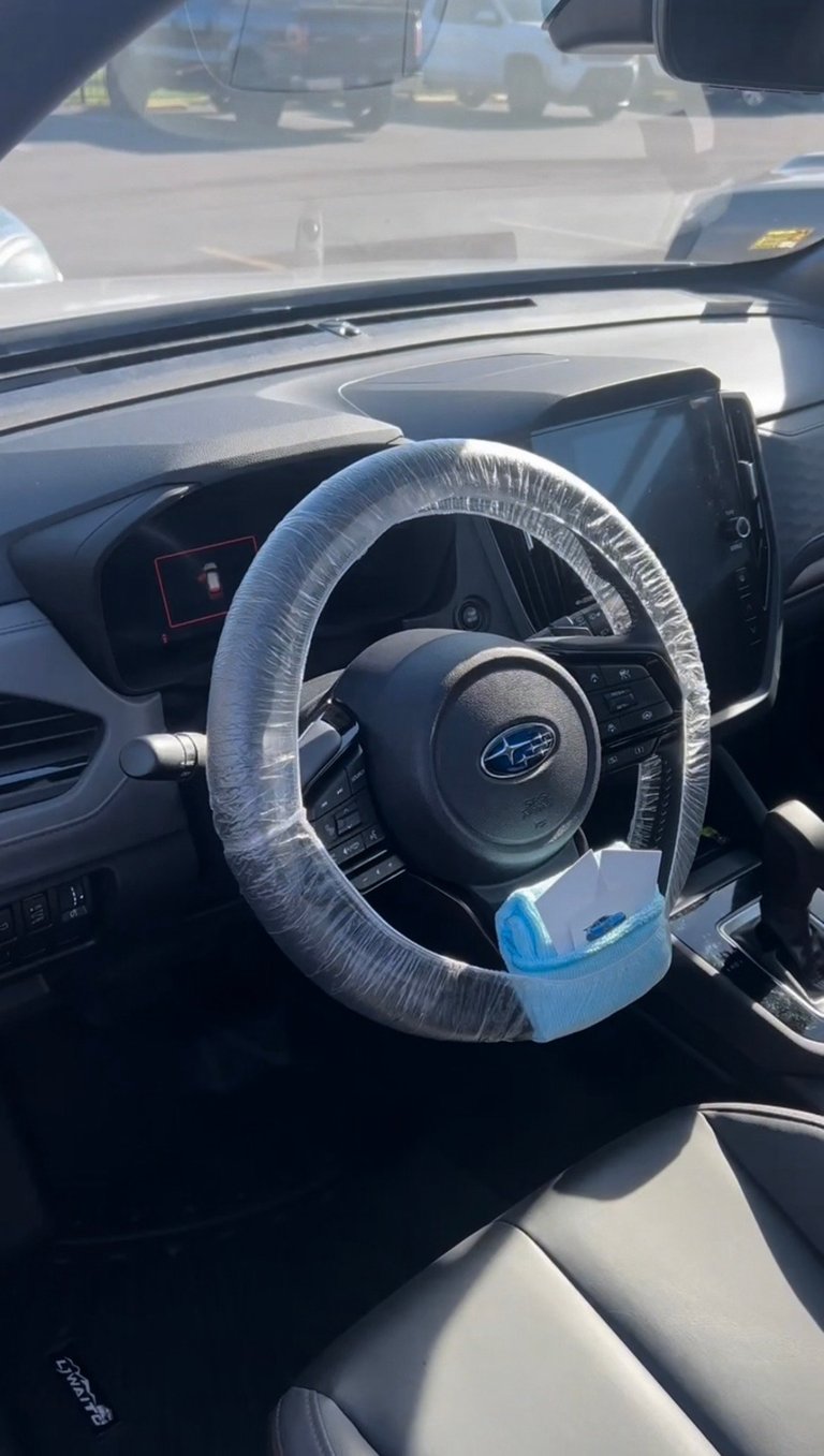 Interior view of a Subaru car showing a steering wheel wrapped in clear plastic protective covering