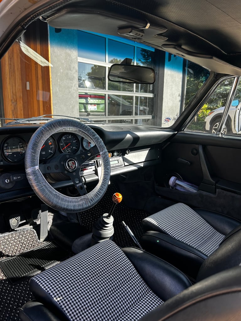 Interior of a classic vintage car with blue steering wheel, dashboard, and checkered seat covers, viewed through windshield