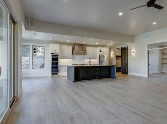 Modern open-concept kitchen and living space with light wood flooring, white cabinetry, dark kitchen island, and stainless steel appliances