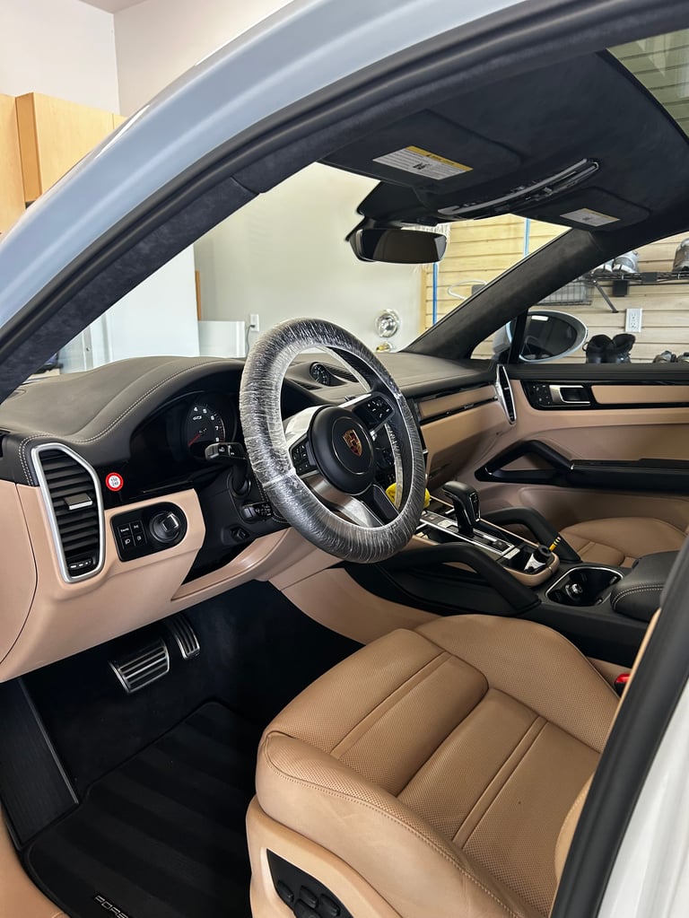 Interior view of luxury sports car with tan leather seats, black steering wheel, and open convertible roof in showroom